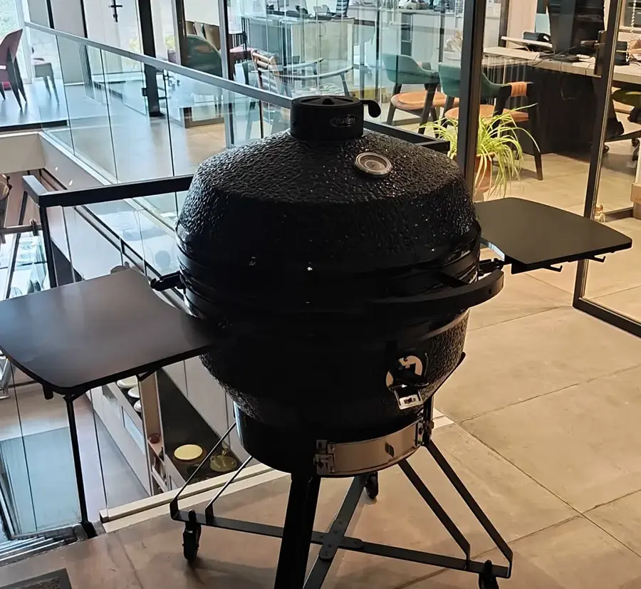 Maximus ceramic kamado grill in matt black textured finish on a wheeled steel stand with folding side shelves, displayed in the Spiteri Catering showroom