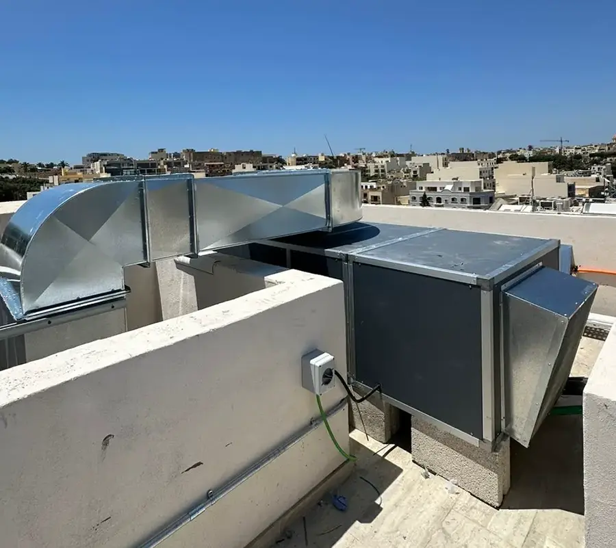 Custom fabricated ductwork at Casa Giuseppe Care Home emerging through the rooftop parapet in Victoria, Gozo, with the town visible behind
