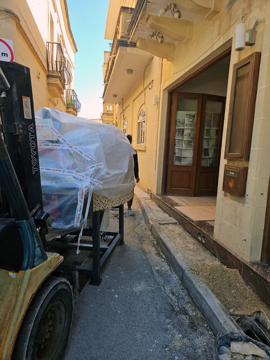 Valoriani Rotante 100 oven still in protective wrapping being moved into the Joe's Street Pizza premises on a pallet jack, with the red-painted alcove visible behind