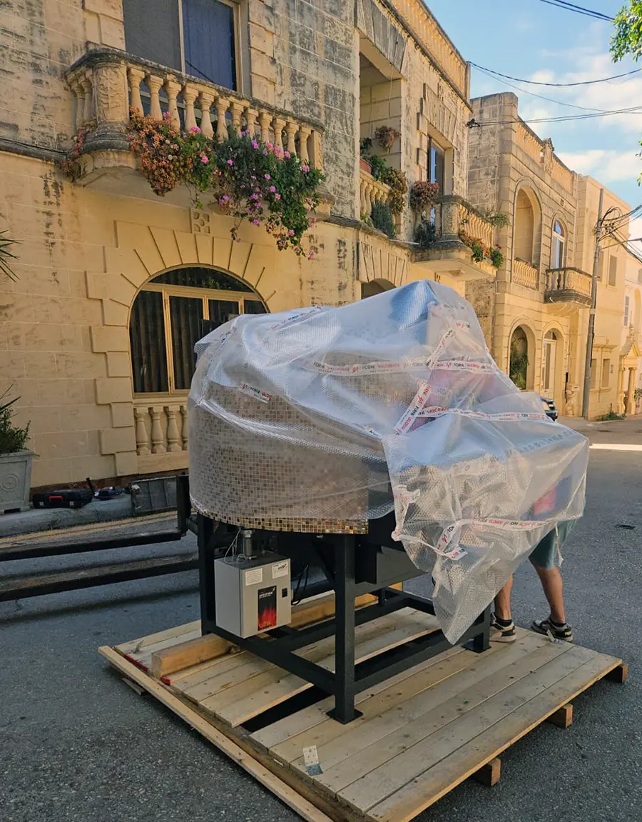 The wrapped Valoriani oven on a forklift being manoeuvred through a narrow Nadur street towards a traditional Maltese limestone doorway