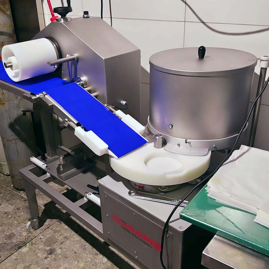 Gesame automatic burger patty forming machine with blue interleaving paper feed installed in a retail prep kitchen